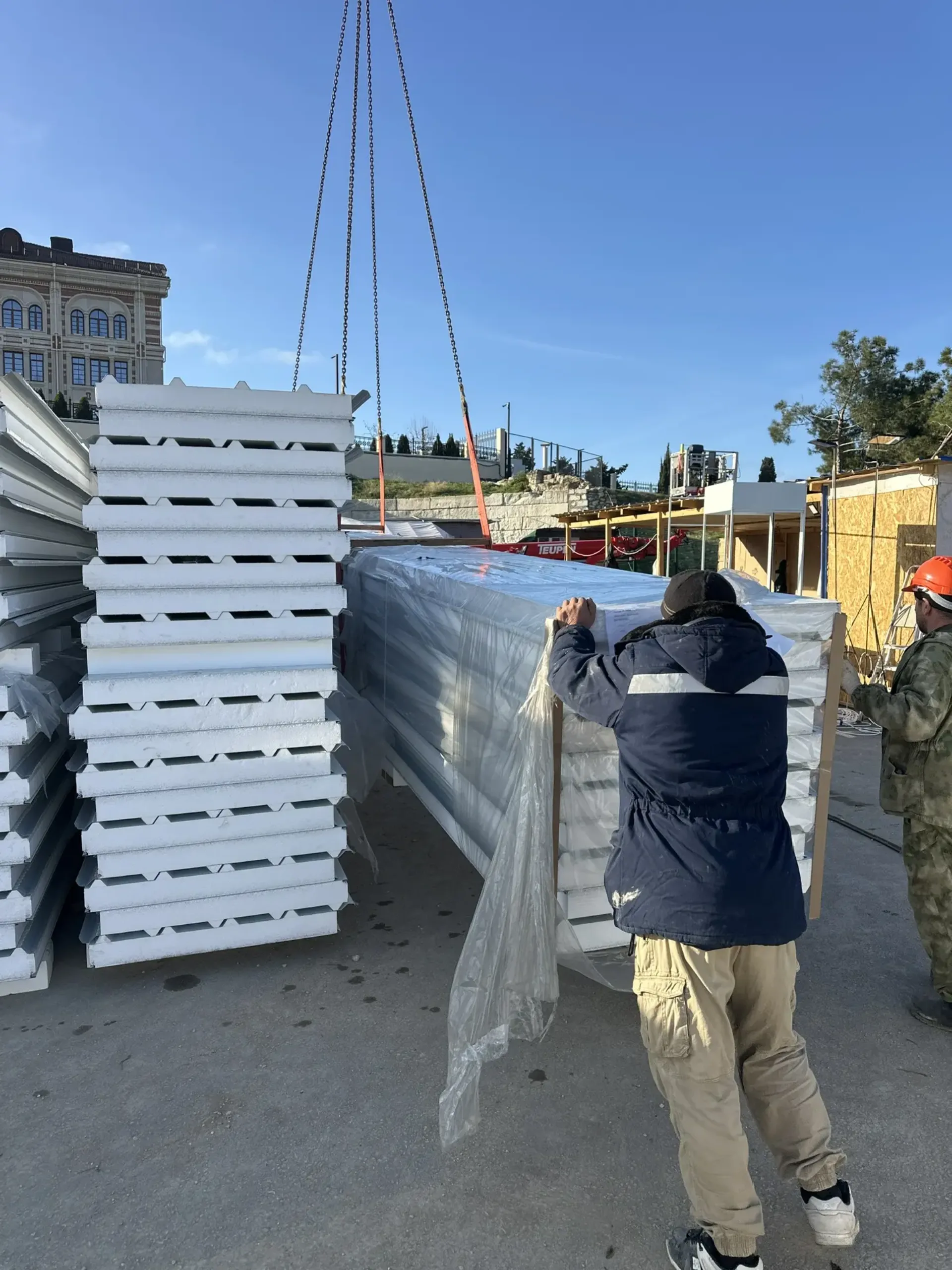 Разгрузка пакета панелей краном на площадке: два человека принимают груз